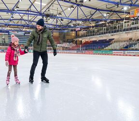 Ein Vater mit seiner Tochter beim Eislaufen in der Eissporthalle